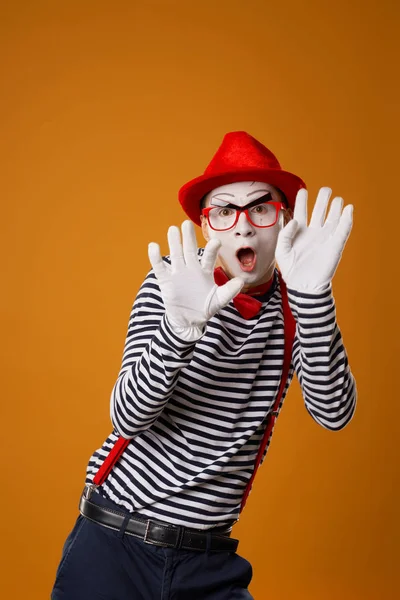 Serieuze mime in witte handschoenen en rode hoed kijkend naar camera op oranje achtergrond — Stockfoto