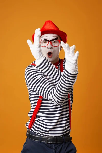 Jonge mime reu in witte handschoenen en rode hoed kijkend naar camera op oranje achtergrond — Stockfoto
