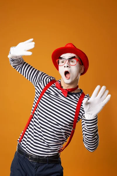 Young mime male in white gloves and red hat looking at side on orange background — 스톡 사진