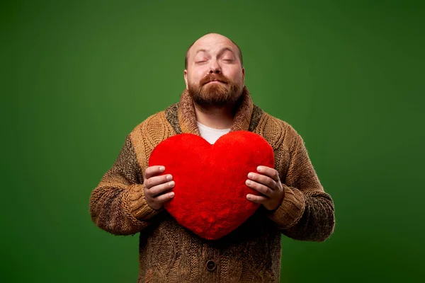Férfi csukott szemmel tartja játék szív közben álló üres zöld háttér — Stock Fotó