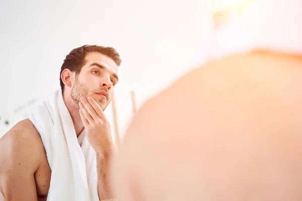 Hombre morena sin afeitar con toalla blanca en el cuello de pie cerca del espejo —  Fotos de Stock