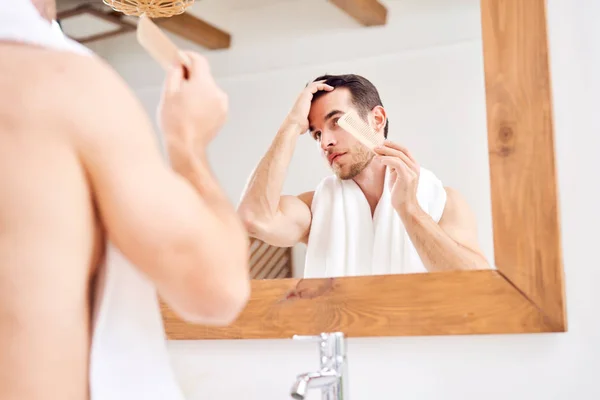 Молодой мужчина гладит волосы, стоя перед зеркалом — стоковое фото