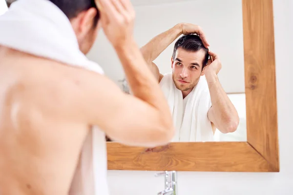 Brunet man combing his hair while standing by mirror in bath — Stock Photo, Image