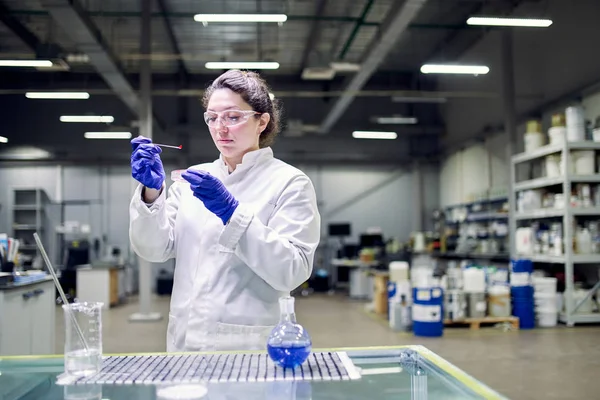 Mujer seria de laboratorio en bata blanca con vidrio experimental en sus manos lleva a cabo experimentos — Foto de Stock