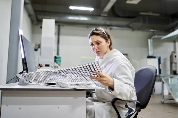 Joven técnico de laboratorio sentado a la mesa con computadora y malla de carbono — Foto de Stock