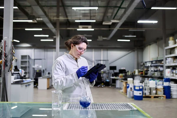 Woman lab assistant with flask and tablet in hands — Stock Photo, Image