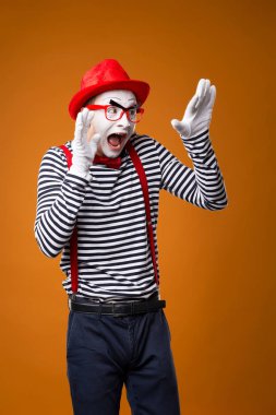 Korkak pandomimci yelekli adam ve turuncu arka planda kırmızı şapka.