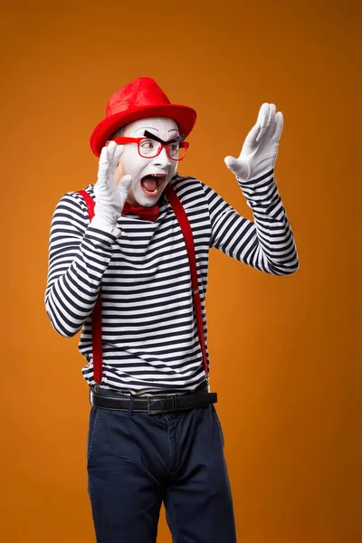 Verängstigter Mime in Weste und rotem Hut auf orangefarbenem Hintergrund. — Stockfoto