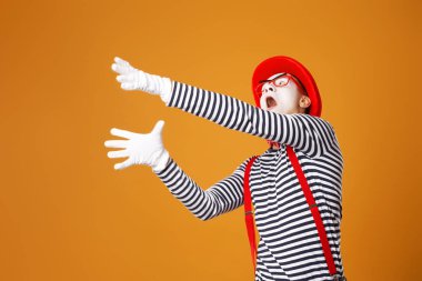 Kırmızı şapkalı üzgün pandomimci ve turuncu arka planda yelek