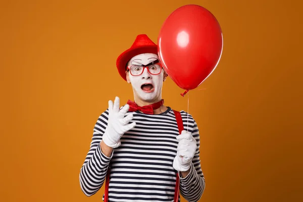 Mimo de palhaço em colete e chapéu vermelho com balão na mão sobre fundo laranja — Fotografia de Stock