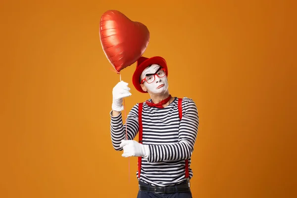 Mime σε κόκκινο καπέλο και γιλέκο κρατά μπάλα καρδιά στα χέρια του, ενώ κοιτάζοντας την κάμερα — Φωτογραφία Αρχείου