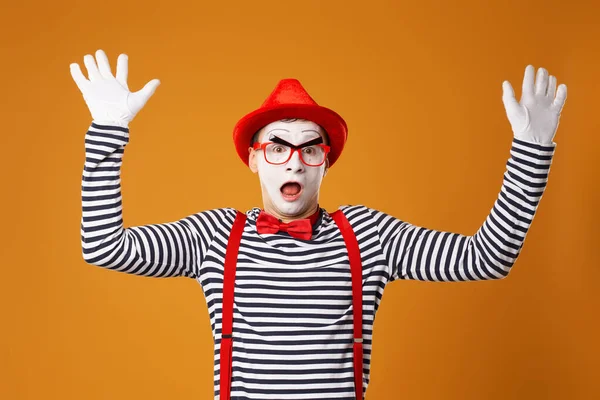 Überraschter Mime mit rotem Hut und Weste mit Händen nach oben auf orangefarbenem Hintergrund — Stockfoto
