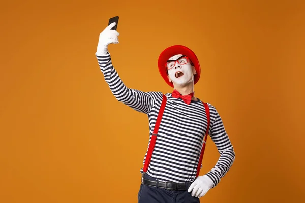 Νεαρός άντρας μίμος με λευκά γάντια και κόκκινο καπέλο βγάζει selfie σε πορτοκαλί φόντο — Φωτογραφία Αρχείου