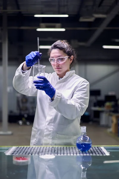 Serious lab girl in glasses and white coat with experimental glass in her hands conducts experiments — Stock Photo, Image