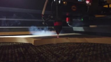 MDF laser cutting machine close up cuts wooden board with red beam.