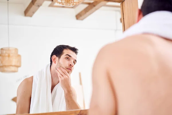 Young man with white towel on neck standing near mirror