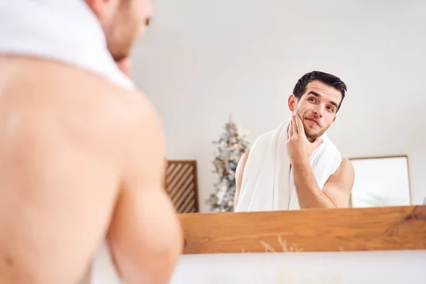 Unshaven nu jovem macho com toalha branca em seu pescoço de pé perto do espelho — Fotografia de Stock