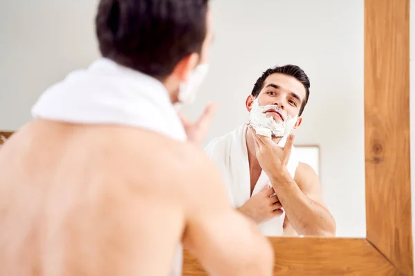 Brunet male with foam on beard near mirror in morning — 图库照片
