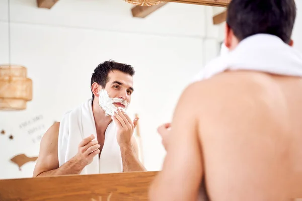 Young male with foam on beard near mirror in morning — Stok fotoğraf