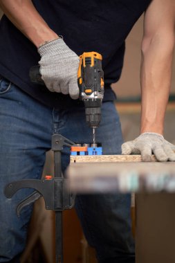 Beyaz eldivenli tanınmayan marangoz atölyede matkap ve tahta kullanıyor.