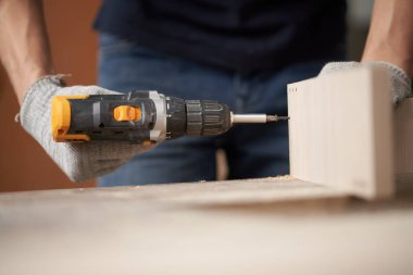 Beyaz eldivenli tanınmayan marangoz erkek atölyede matkap ve tahta kullanıyor.