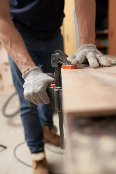 Hombre carpintero en guantes blancos abrazaderas tablero en vicio en el taller — Foto de Stock