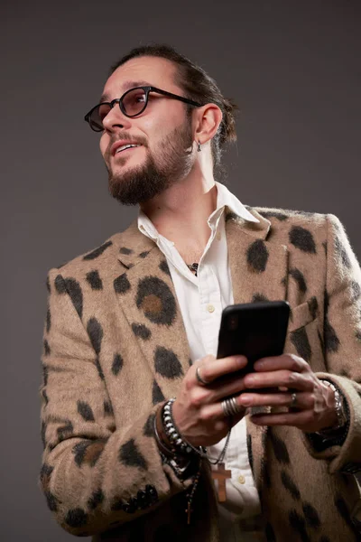 Hombre con gafas de sol en chaqueta mirando a un lado con el teléfono en las manos sobre fondo marrón — Foto de Stock