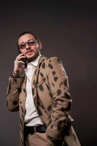 Счастливый мужчина в солнечных очках в куртке разговаривает по телефону на коричневом фоне — стоковое фото