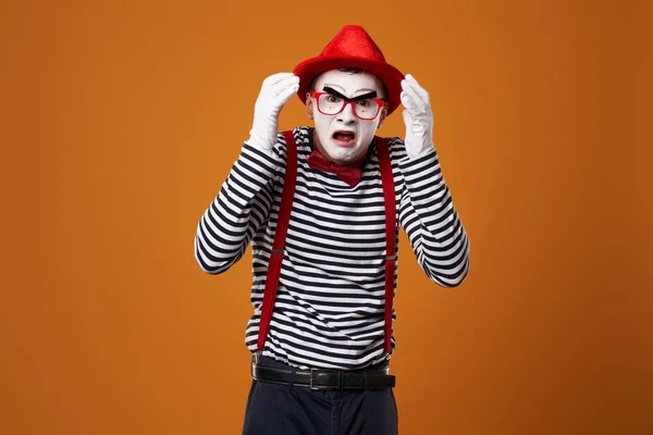 Sorgsen mima i väst och röd hatt på orange bakgrund — Stockfoto