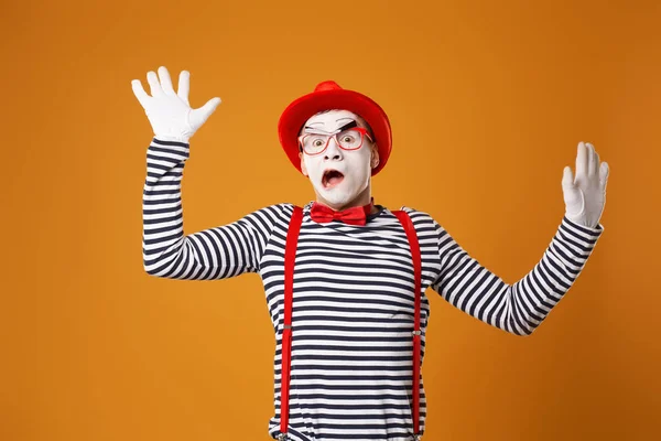 Meglepett pantomim férfi piros kalapban és mellényben feltartott kézzel narancs alapon — Stock Fotó