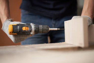 Unrecognizable carpenter man in white gloves with drill and board in workshop