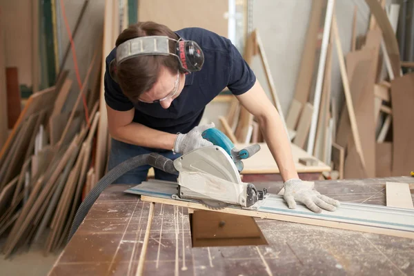 Carpenter in protective headphones and white gloves works on jigsaw in workshop — ストック写真