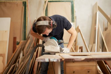 Güvenlik gözlüklü ve beyaz eldivenli işçi atölyede yapboz üzerinde çalışıyor.