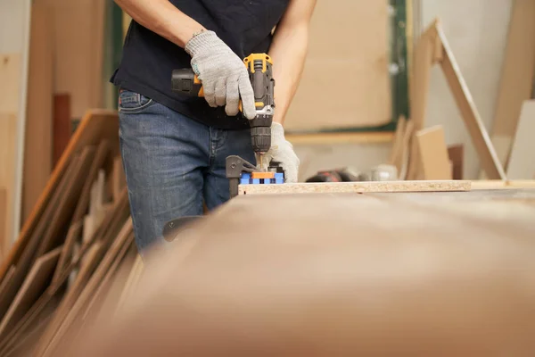 Человек плотник в белых перчатках с дрелью и доской в мастерской — стоковое фото