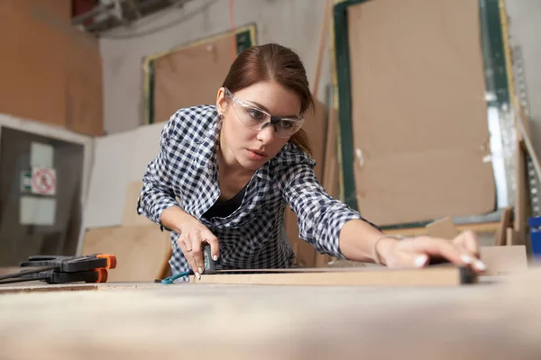 Meisje houtbewerker in bril met houten plank achter werkbank — Stockfoto