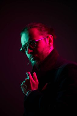 Siyah arka planda gözlüklü, sakallı genç bir erkek.