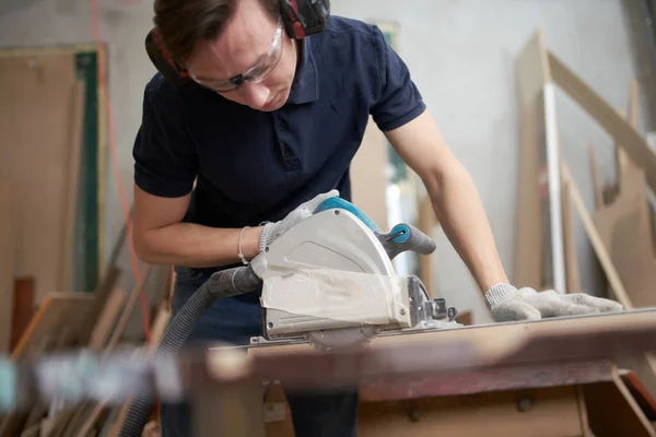 Male in safety glasses and white gloves works on jigsaw in workshop — Stock fotografie