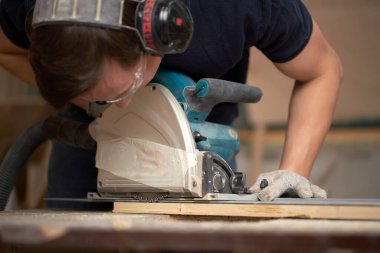 Carpenter male in white gloves works on jigsaw in workshop