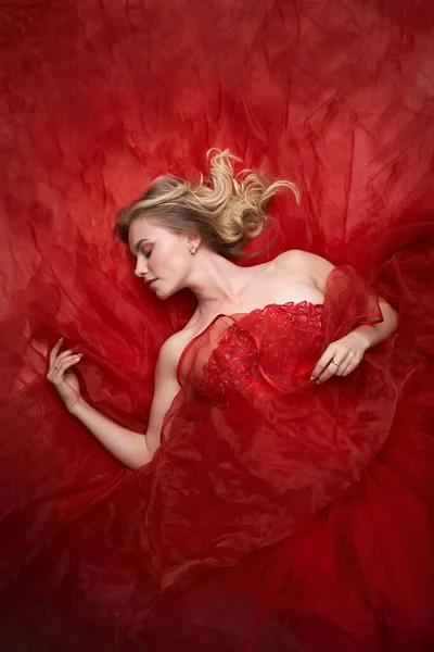 Young blonde in red dress lying in studio — Stock Photo, Image