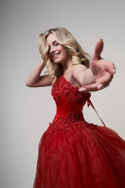 Щаслива блондинка в довгій червоній сукні з простягнутою рукою в студії — стокове фото