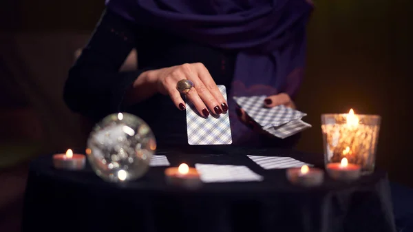 Close-up of woman fortuneteller hand with cards while sitting at table with candles in dark room — Stock Photo, Image