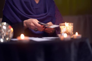 Falcı kadına yakın çekim. Kartlarla kehanette bulunuyor. Masada yanan mumlarla, sihirli topla oturuyor.
