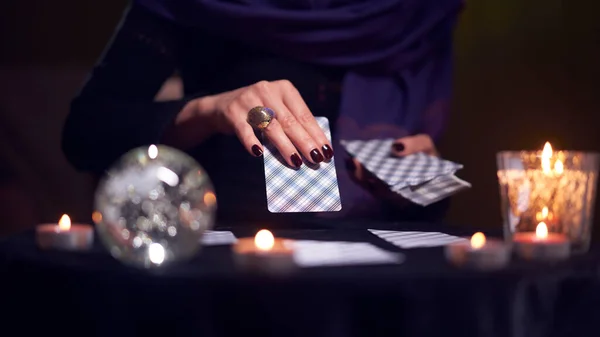 Close-up of fortuneteller hands with cards while sitting at table with candles in dark room — Stock Photo, Image