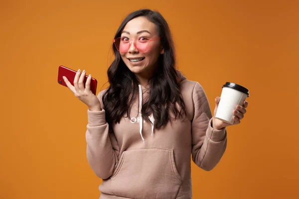 Азиатская брюнетка в розовых очках с телефоном в руках и стеклом, изолированным в студии — стоковое фото