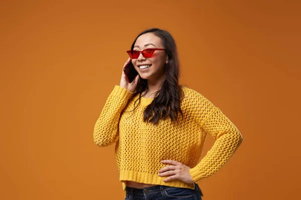 Χαρούμενη γυναίκα με κόκκινα γυαλιά που μιλάει στο τηλέφωνο σε λευκό πορτοκαλί φόντο — Φωτογραφία Αρχείου
