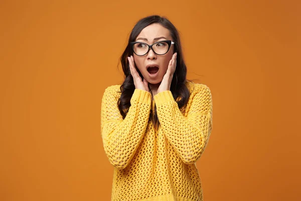 Confused woman in glasses on empty orange background — Stock Photo, Image