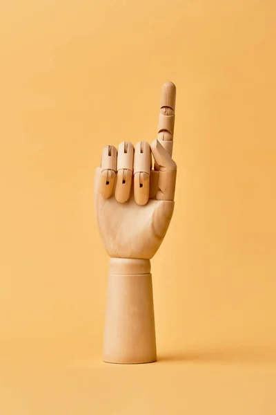 Mão humana de madeira com o dedo levantado no fundo laranja — Fotografia de Stock