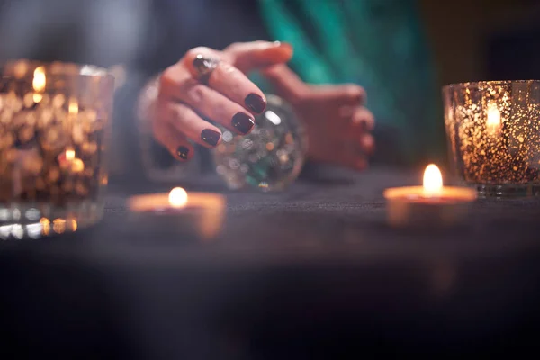 Zbliżenie wróżki w zielonej sukience dyskutującej na magicznym stole kulkowym z palącymi się świecami — Zdjęcie stockowe