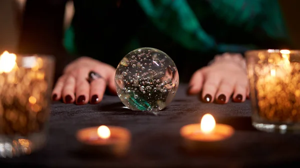 Fortuneteller divining on magic ball at table with burning candles