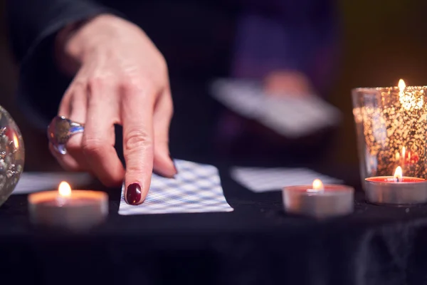 Primer plano de adivinos mano con tarjetas de adivinación en la mesa con velas en la habitación oscura —  Fotos de Stock